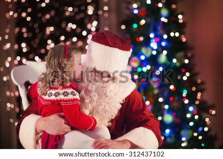 Santa Claus and children opening presents at fireplace. Kids and father in Santa costume and beard open Christmas gifts. Little girl helping with present sack. Family under Xmas tree at fire place.