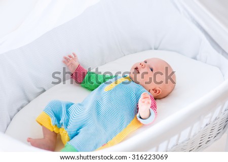 Newborn baby boy playing in bed on a sunny morning. New born child relaxing in bassinet. Children sleep. Bedding and clothing for kids. Infant napping in bed. Healthy little kid shortly after birth.