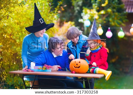 Happy family carving pumpkin at Halloween. Dressed up child trick or treating. Kids and parents trick or treat. Child in witch costume playing in autumn park. Toddler kid with jack-o-lantern.