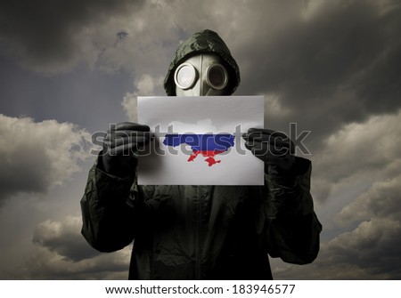 Man wearing a gas mask on his face and holding white paper and Ukraine map with Russian flag.