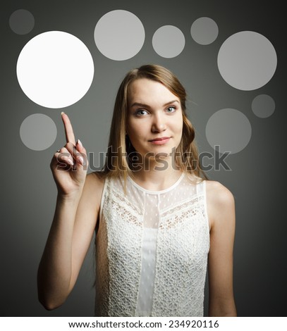 Girl in white pointing at something interesting on grey background. Girl having an idea with grey bubbles over her head.