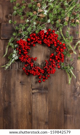 green christmas tree branches and wreath from red berries over rustic wooden background. festive decoration