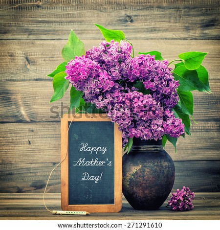 Lilac flowers in vase on wooden background. Blackboard with sample text Happy Mother\'s Day! Retro style toned picture