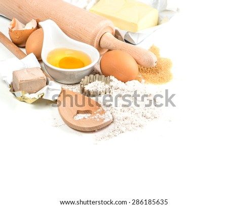 Baking ingredients flour, eggs, yeast, sugar, butter. Wooden kitchen utensils spatula and rolling pin. Food preparation