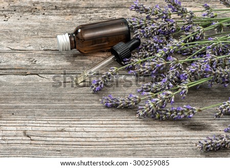 Perfumed herbal oil essence and dried lavender flowers on wooden background. Selective focus
