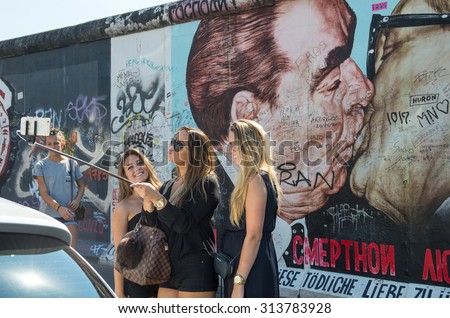 BERLIN, GERMANY - AUGUST 30, 2015: Cute young people taking selfie pictures on the famous Berliner Mauer. Graffiti at the East Side Gallery in Berlin, Germany