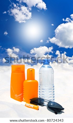 sun protection cream, water and sunglasses over blue sky