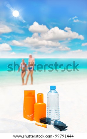 sun protection cream, bottle of water and sun glasses on beach and blue sky background