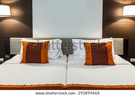 Red pillow on bedroom with white bed sheet and lamp light on
