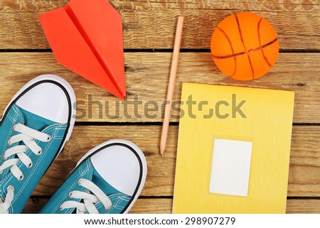 sneakers with paper plane, notebook and basketball on wooden surface