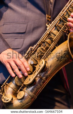 Man playing a brass tenor saxophone or sax during a live performance in an orchestra, a popular reed instrument in jazz, blues and country music