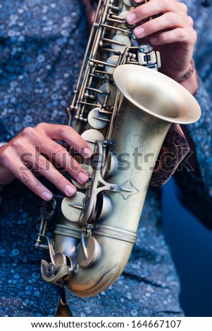 Saxophonist playing a saxophone in an orchestra during a live performance, close up view of his hands manipulating the valves