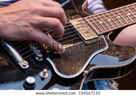 Close up of the hands of a man plucking the strings on a decorative wooden electric guitar with focus to the pickup and strings