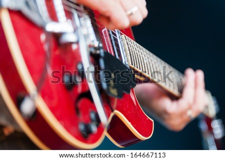 Close up view of a male guitarist playing an electric guitar with focus to the pickup of the guitar and the strings