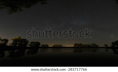 Smooth surface of forest lake on a background of the night sky and the Milky Way.
