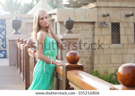Beautiful blond woman in green dress standing on bridge in tropical country