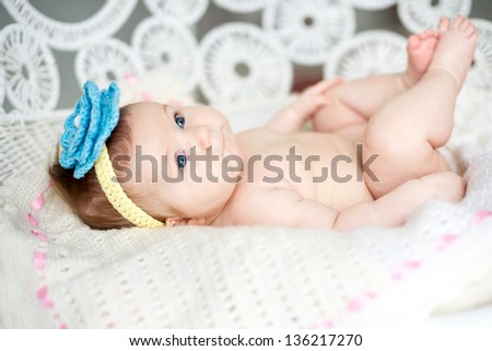 Adorable newborn girl lies on white plaid in lace armchair with blue flower on head