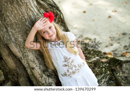 Pretty european blond girl sitting on huge tree in tropical garden