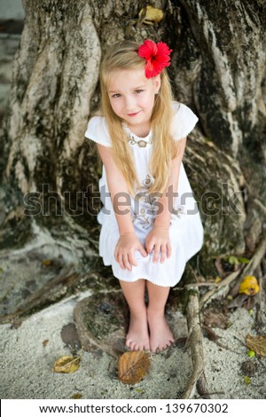 Pretty european blond girl sitting on huge tree in tropical garden and dreaming
