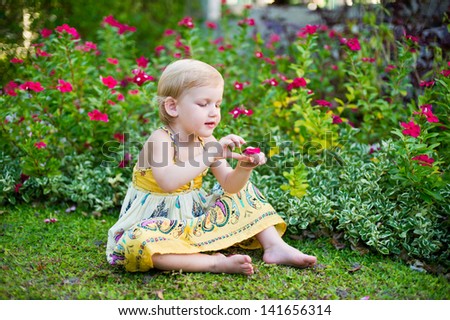 Adorable little girl in dress sitting in tropical blooming garden plays with flowers
