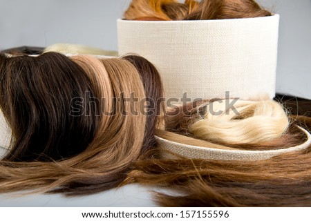 Locks of faux hair for beauty saloon different colors and structure in box. Blond, red and brunette on gray background