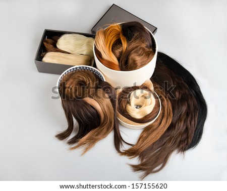 Locks of faux hair for beauty saloon different colors and structure in box. Blond, red and brunette on gray background
