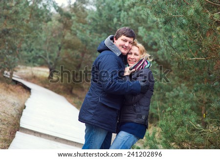 Young happy couple european man and woman holding each other in autumn forest with green pines and wood road