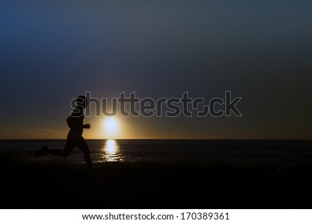 A silhouette of jogger at a grassy path along the ocean.
