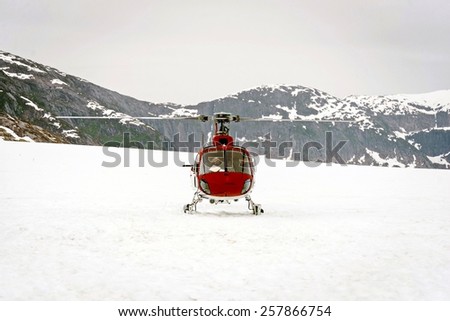 Helicopter landing on glacier in between snowy mountains for glacier tours during the winter months.