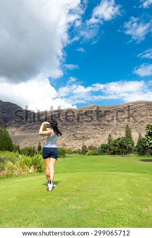 Female golfer hits golf ball towards mountains and cloudy skies with a driver