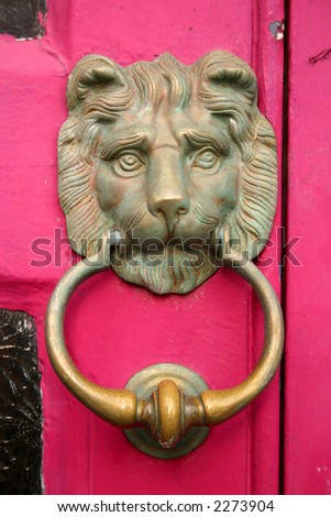 Old brass lion door knocker on a pink door.