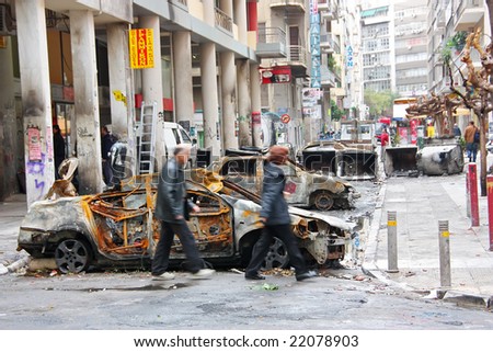 ATHENS (GREECE) - December 15: People passing by burnt cars in an Athens downtown street during the big riots caused by the death of a teenage student after being shot by a policeman