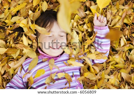 Young Girl in a Pile of Autumn Leaves, Eyes Closed as Leaves Fall on Her