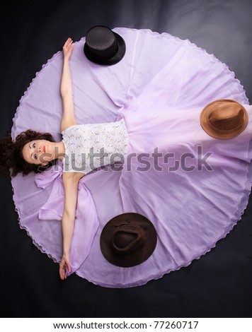 Attractive woman lying on the floor in liliac dress with a three hats