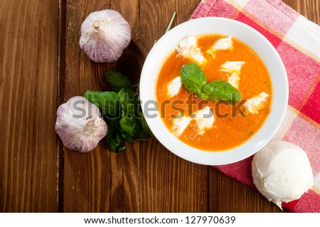 Tomato soup with shredded cheese in ceramic bowl on a wooden table.