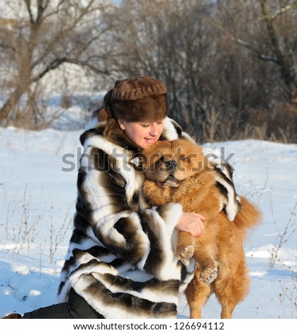 The woman in a mink fur coat plays with a dog. Winter weather