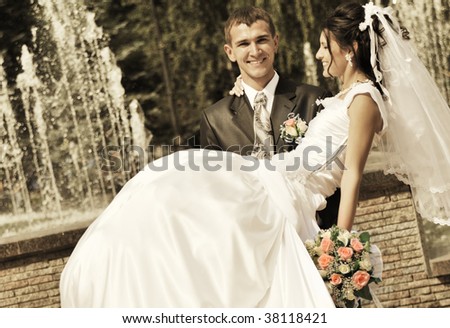 The groom holds the bride on hands. A happy newly-married couple on a background of a fountain