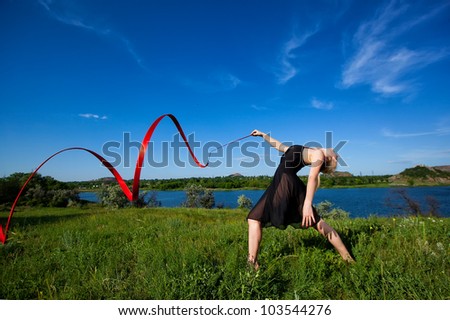 Young gymnast doing gymnastic exercises with red ribbon outdoor