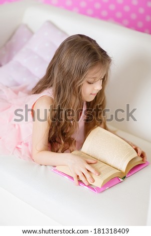 Portrait of 6 years old child reading book at at bright pink room