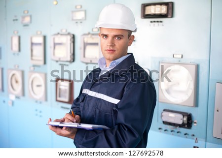 Portrait of young smiling engineer taking notes in control room
