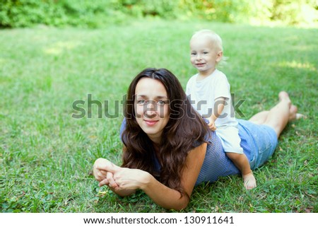 Portrait of a mother lying on the lawn with her son sitting on her back, in the outdoors.