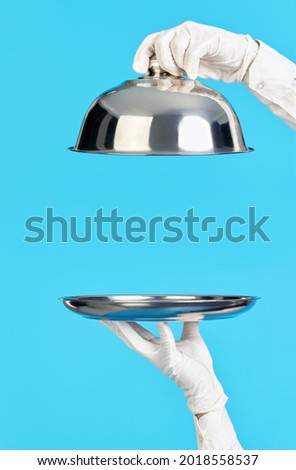 Elegant waiter's hands in white gloves holding silver tray and cloche on blue background. Restaurant, horeca, first class service concept Photo stock © 