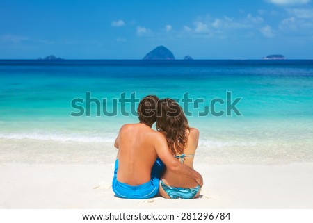 Young honeymoon couple sitting together on a sandy tropical beach