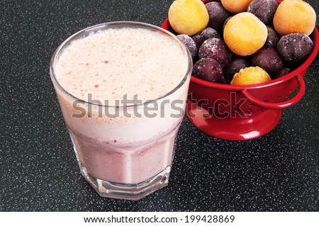 Cherry milk shake in a glass cup  and a red colander with frozen cherries and cherry-plum on a dark background