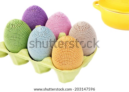 Colorful crocheted eggs in a light green carton egg box on a white background