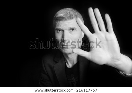 Grey-haired man in suit and  black T-shirt at the age of forty-six years old  with hand  looking at the camera on a black background