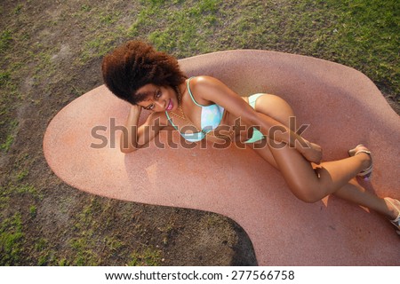Attractive young female laying on a abstract park bench in her bikini
