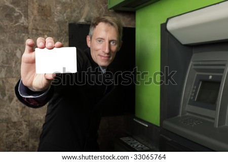 Businessman holding a blank card by an atm machine