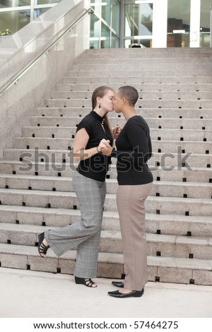 Two young businesswomen kissing by an office building