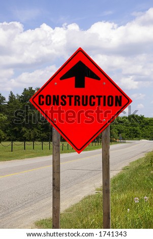 Bright Orange Reflective Construction Road Sign against a blue sky background on the side of a country rural road